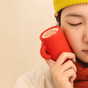 Roter USB-Handwärmer im Becherdesign mit Seitengriff, an die Wange einer Frau gehalten