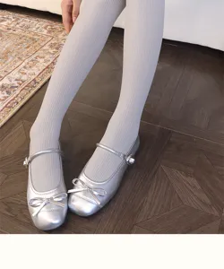 Close-up of fine vertical ribbing on pale tights, styled with silver bow Mary Jane flats