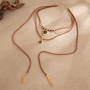Detail van gelaagde bruine koorden met gouden hart- en ovale hangers en kwastjes van kettinkjes