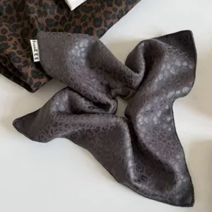 Detalle de un pañuelo gris para el cabello, efecto satén, con jacquard de leopardo y bordes cosidos
