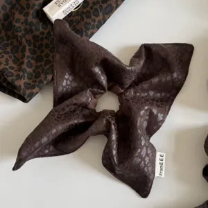 Vista extendida de tela marrón oscuro tipo satén, con discreto estampado de leopardo y bordes cosidos