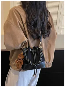 Back view of a black bucket bag with braided handles, drawstring closure and brown bear charm