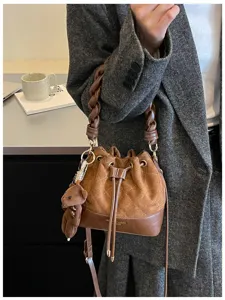 Brown suede bucket bag with diamond stitching, braided handle and bear charm shown in an outfit