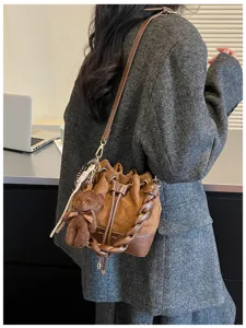 A brown quilted bucket bag with drawstring top, chunky handle and bear charm worn over a tweed coat
