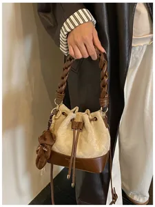 Close-up of a beige and brown bucket bag with a braided handle, drawstring and teddy bear charm