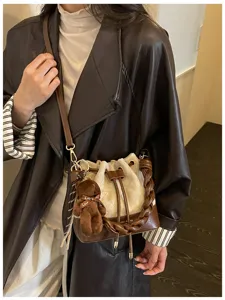 Model wearing a brown and cream bucket bag with braided handle, drawstring closure and teddy charm