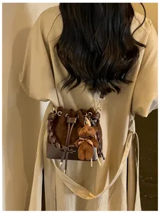Back view of a brown suede bucket bag with woven chain handle, drawstring closure and teddy charm