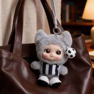 Gray cat-eared plush doll keychain with striped outfit and soccer-ball charm on a brown bag