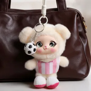 Plush bear keychain with a soccer ball charm hanging against a dark brown leather handbag