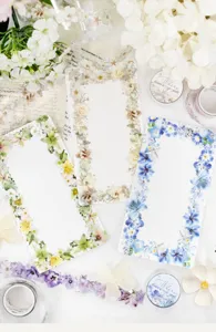 Overhead view of three floral-bordered memo sheets arranged with flower-patterned tape on fabric
