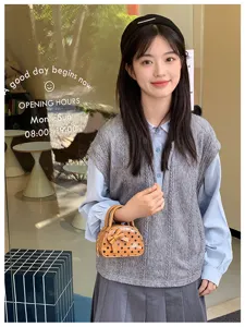 Model holding a small brown polka-dot handbag with a bow, styled with a gray knit vest