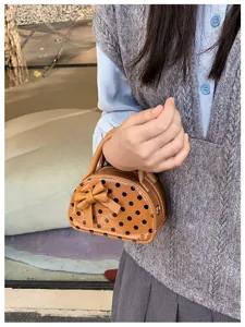 A child holds a tan polka-dot mini bag with a bow and zipper against a casual outdoor backdrop