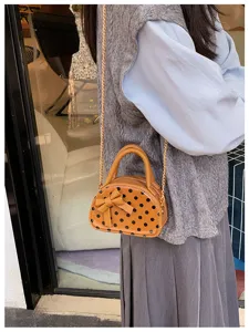 A small orange bag with black dots and a bow, worn with a gold chain over a gray outfit