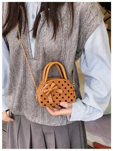 Close-up of a brown polka-dot mini bag with a bow and gold chain, held against a knit outfit