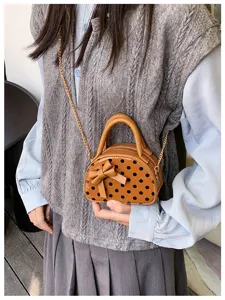 Close-up of a brown half-moon bag with black dots and bow, held with its gold chain strap
