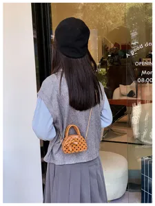 Rear view of a small orange polka-dot bag with a bow and chain strap worn across the body.