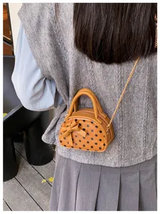 Worn at the waist, this view shows a brown polka-dot bag with a bow and gold chain strap.