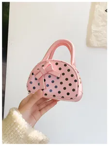 Handheld close-up of a pink polka-dot mini bag with a raised bow, curved handle and zip opening