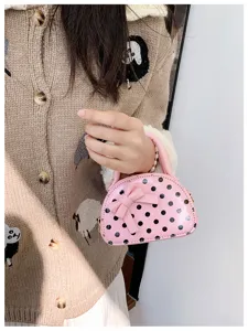 Close-up of a pink dome bag with black polka dots and a bow, held by its top handle
