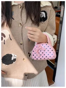 Pink polka-dot mini handbag with a bow, held by hand against a beige knit cardigan
