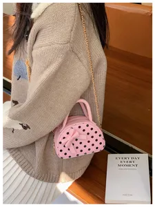 A small pink polka-dot bag with a bow and gold chain worn over a beige sweater in a lifestyle scene