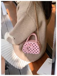 Pink polka-dot mini handbag with bow and gold chain worn over a beige sweater and white skirt