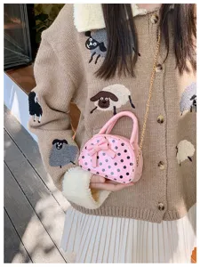 Lifestyle view of a pink polka-dot mini bag with bow and gold chain, held against a knit outfit