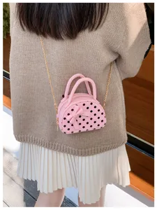 Small pink polka-dot bag with a bow and gold chain, worn over a knit top and pleated skirt