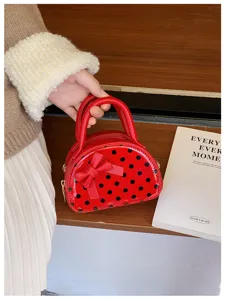 Close-up of a glossy red mini handbag with black polka dots and a bow, held by its handles