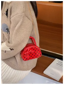 Small red polka-dot purse with bow and gold chain, worn over a beige knit cardigan