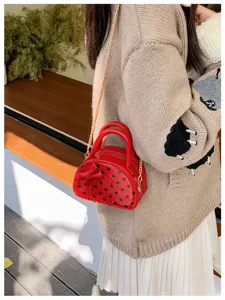 Side view of a red polka-dot mini bag with a bow and gold chain worn over a knit sweater