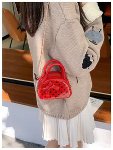 Side view of a red polka-dot mini bag with bow detail and gold chain strap worn over a sweater
