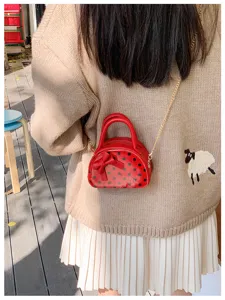 Close-up of a red polka-dot mini bag with bow and gold chain worn over a knit sweater