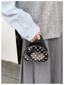 Close-up of a hand holding a glossy black mini bag with white dots and a bow detail