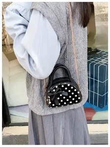 A black mini bag with white polka dots and a bow, worn on a gold chain in a street setting