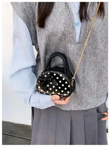 Close-up of a black polka-dot mini bag with a bow and gold-tone chain, worn over a gray vest.