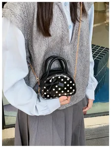 Close-up of a polka-dot mini bag with a bow and gold chain, carried against a gray outfit