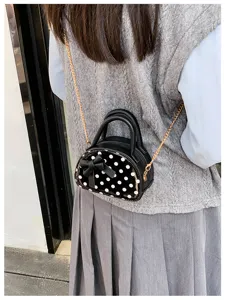 Black-and-white polka dot mini bag with a bow and gold chain, worn over a grey outfit