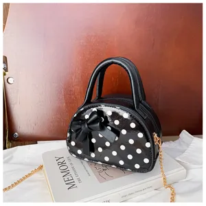 Black glossy bag with white polka dots, a bow and gold chain, displayed on a book