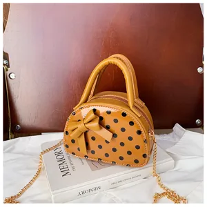Glossy orange mini bag with black polka dots and bow, shown on a book with its gold chain strap