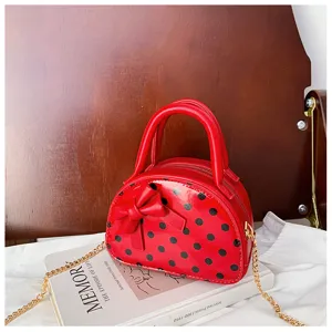Detail view of a red glossy polka-dot mini bag with a bow and gold chain, displayed on a book