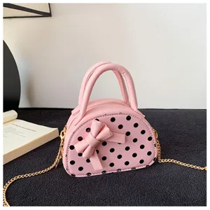 Close-up of a pink dotted bag with a sculpted bow, twin handles, and a gold chain strap