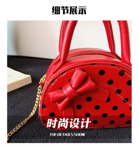 Close-up of a red bag with black polka dots, a decorative bow, zipper edge and gold chain strap