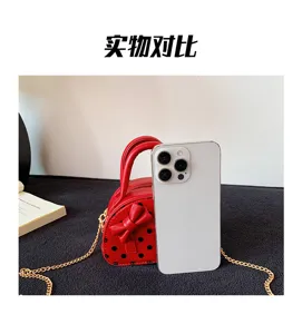 Small red bag with black polka dots and a bow, shown beside a phone for size comparison