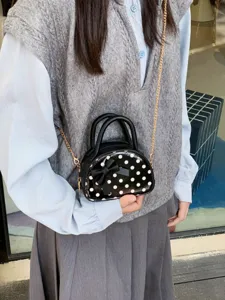 Girls' black polka-dot mini handbag with bow and gold chain, shown worn as a crossbody bag