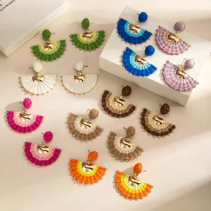 Flat lay of colorful woven fan earrings with gold-tone accents arranged on a cream surface