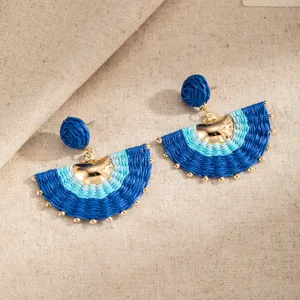 Pair of blue fan-shaped woven earrings with gold bead accents, displayed on beige linen fabric.