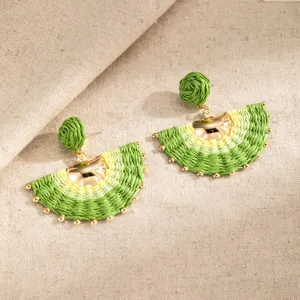 Pair of fan-shaped woven earrings in green and pale yellow, with gold beads on beige linen
