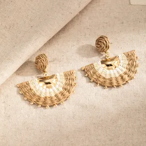 Pair of cream and khaki woven semicircle earrings with gold bead accents on textured linen