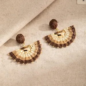 Close-up of two semicircular woven earrings in brown, tan and ivory, with small gold accents